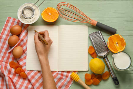 Woman writing in recipe book on color wooden background