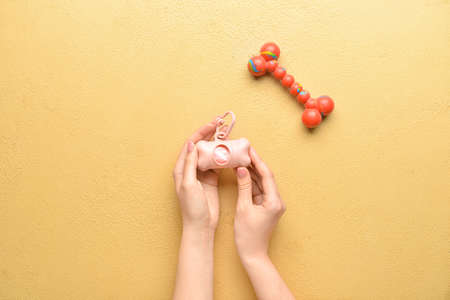 Female hands with pet waste bags and toy on color background, closeup