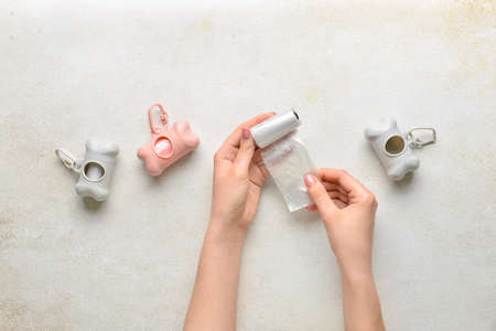 Female hands with pet waste bags and dispensers on light background
