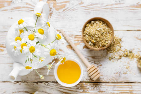 Teapot of fresh chamomile tea with honey and flowers on light wooden backgroundの写真素材