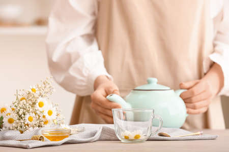 Woman with teapot of tasty chamomile tea on tableの写真素材