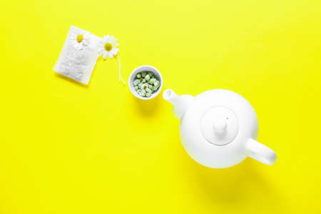 Teapot, chamomile flowers and tea bag on yellow backgroundの写真素材