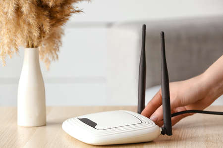 Woman inserting wire into wifi router on table in room