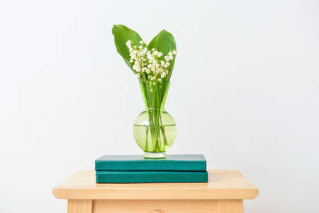 Vase with lily-of-the-valley flowers and books on table near white wallの写真素材