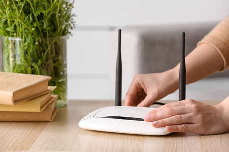 Woman inserting  wire into wifi router on table in roomの写真素材