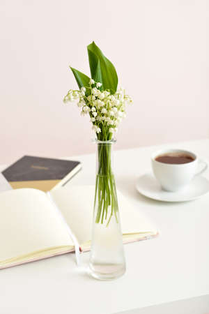 Vase with lily-of-the-valley flowers and books on table