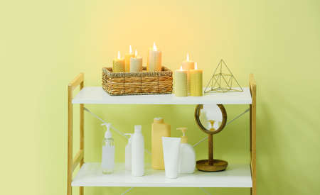 Shelves with burning candles and cosmetics near color wall