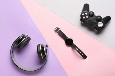 Modern headphones, smart watch and joystick on color background