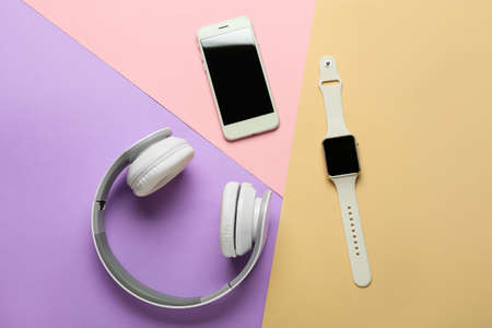 Modern headphones, smart watch and mobile phone on color background
