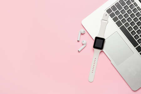Smart watch, earphones and laptop on pink background