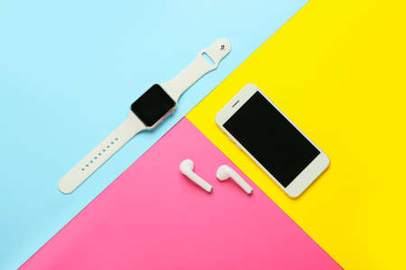 Modern earphones, mobile phone and smart watch on color background