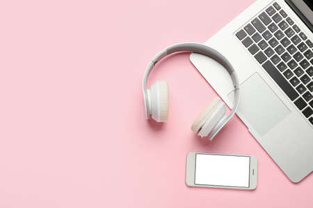 Modern headphones, mobile phone and laptop on pink background
