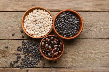 Bowls with different types of beans on wooden background