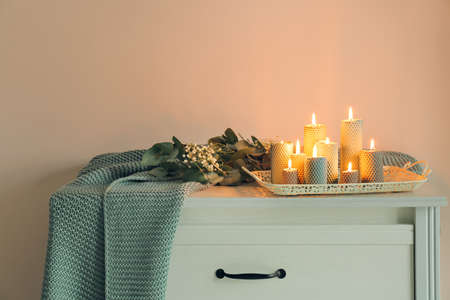 Tray with burning candles and beautiful flowers on chest of drawers in room