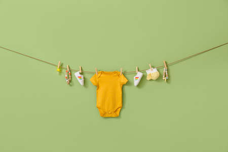 Stylish baby clothes, shoes and accessories hanging on rope against color backgroundの写真素材