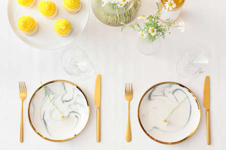 Stylish table setting, cupcakes and chamomile flowers on light background