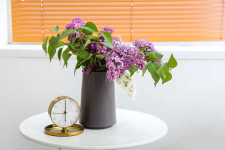 Clock and glass with lilac flowers in interior of light living roomの写真素材