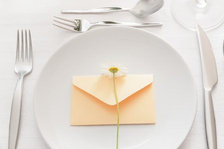 Stylish table setting, envelope and chamomile flower on light backgroundの写真素材