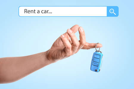 Male hand with automobile key on blue background. Rent a car