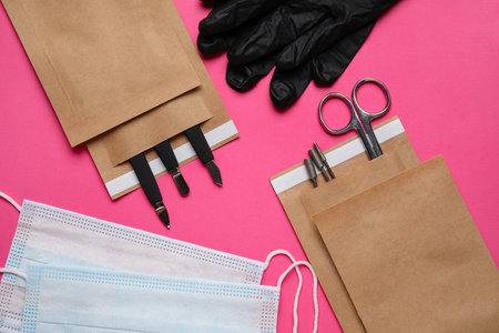 Paper bags with manicure equipment, medical masks and gloves on color background