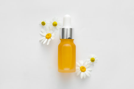 Bottle of essential oil and chamomile flowers on white backgroundの写真素材
