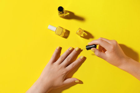 Woman doing manicure on yellow backgroundの写真素材