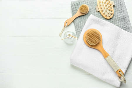 Different massage brushes and towels on light wooden background