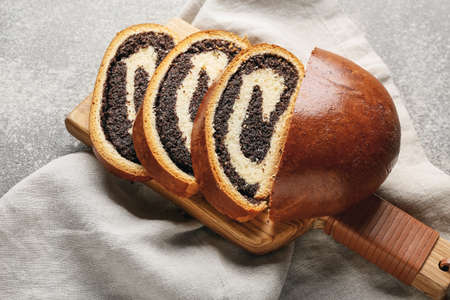 Wooden board with tasty cut poppy seed bun on tableの写真素材