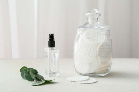 Glass jar with clean cotton pads and bottle of cosmetic product on light tableの写真素材