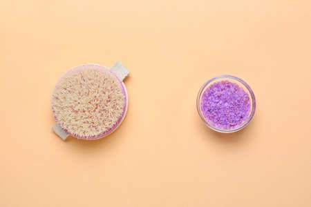 Massage brush and sea salt on color background