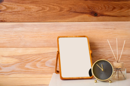 Mirror and stylish alarm clock on chest of drawers near wooden wallの写真素材