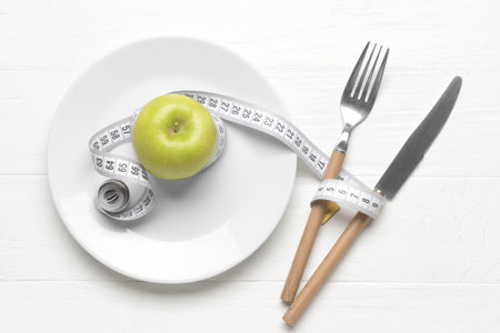 Plate with ripe apple, measuring tape and cutlery on light wooden backgroundの写真素材