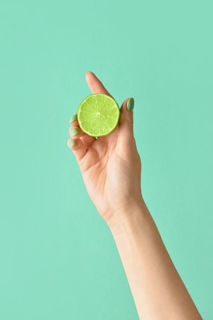 Female hand with lime on color backgroundの写真素材