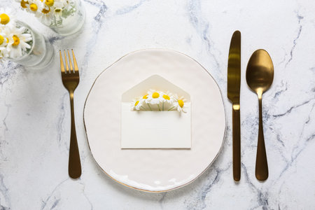 Beautiful table setting with wedding invitation and chamomile flowers on light background