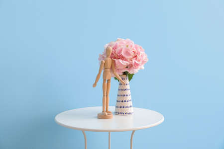 Vase with hydrangea flowers and mannequin on table near color wall