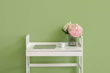 Vase with hydrangea flowers and laptop on table near color wallの写真素材