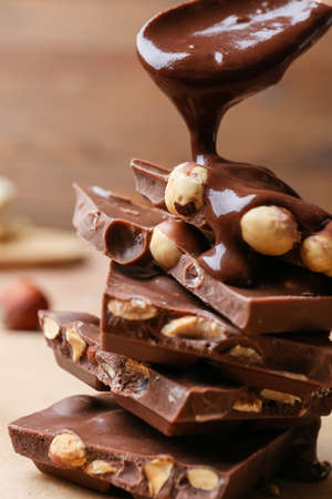Pouring of liquid chocolate onto pieces with nuts on table, closeupの写真素材