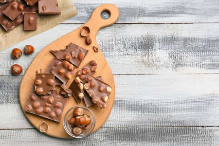 Board with pieces of tasty chocolate and hazelnuts on tableの写真素材