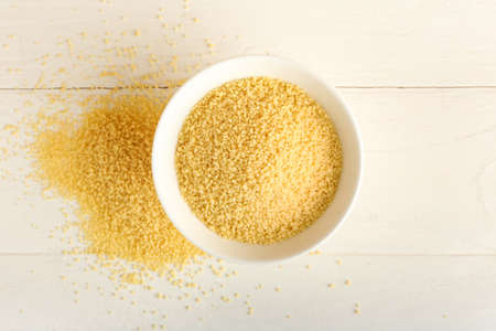 Bowl of raw couscous on white wooden background