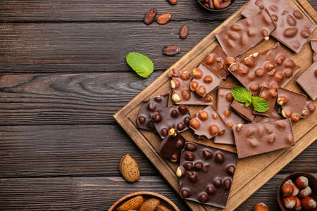Board with pieces of tasty chocolate and nuts on table