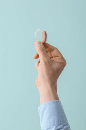 Male hand with hearing aid on color background
