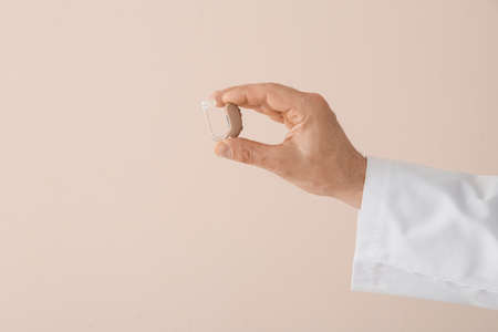 Hand of doctor with hearing aid on light background