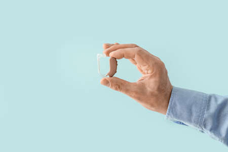 Male hand with hearing aid on color background