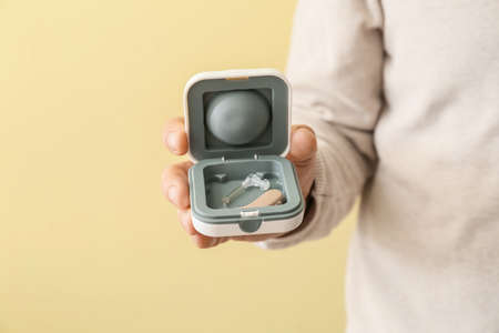 Doctor with hearing aid on color background, closeup
