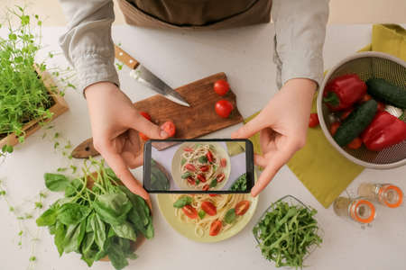 Woman making photo of tasty pasta on light backgroundの写真素材