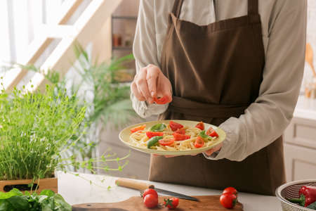 Woman decorating tasty pasta with tomatoes at table in kitchen