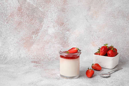 Glass with tasty strawberry panna cotta and mint on light background