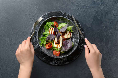 Woman eating tasty fresh salad on dark backgroundの写真素材