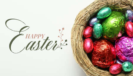 Nest with colorful chocolate eggs and text HAPPY EASTER on white background