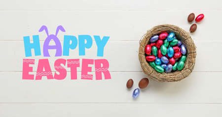 Nest with chocolate eggs and text HAPPY EASTER on white wooden backgroundの写真素材